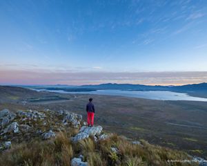 A person stands overlooking a vast landscape at dusk.