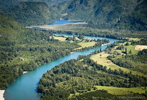Aerial view of a blue river winding through densely forested lands and mountains.