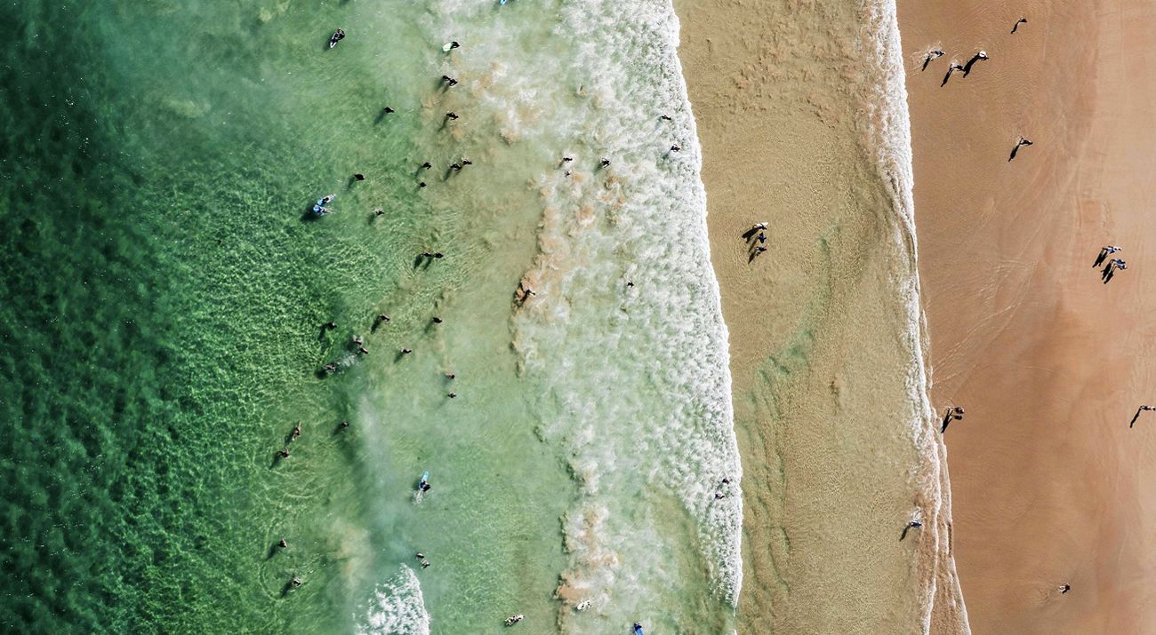 aerial of a lively ocean shore and beach. beachgoers are in the water and on shore.