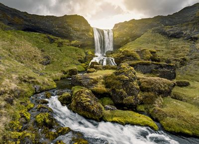 Water spills over a mountain and curves along its slope rushing over mossy green rocks.