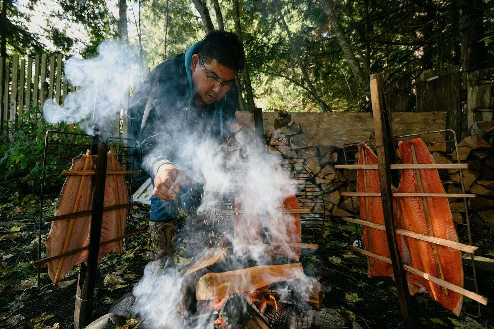 Chief Nanus (aka Mike Tallio) adds wood to a fire as he cooks and smokes butterflied spring salmon in preparation for a Nuxalk potlatch, in Bella Coola, Canada.