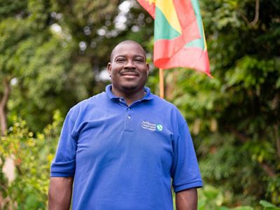 Orlando Harvey smiles as he stands in front of bright green trees.
