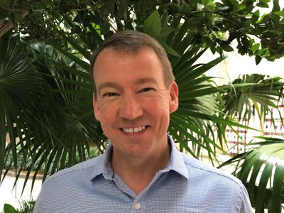 Rob Brumbaugh stands smiling in front of palm trees.