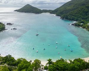 Aerial view of a Seychelles harbor, with beach, boats and islands in background.