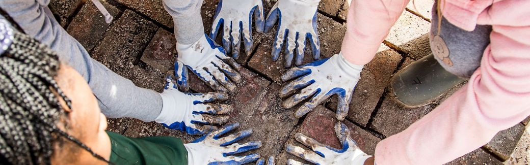 A group of young people crouch on the ground placing their hands in a circle on the ground.