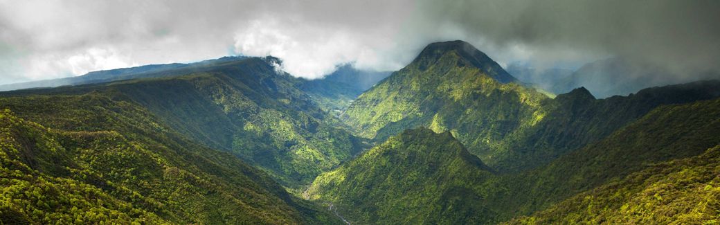 An aerial view down a deep mountain valley with heavily forested ridges rising on either side.