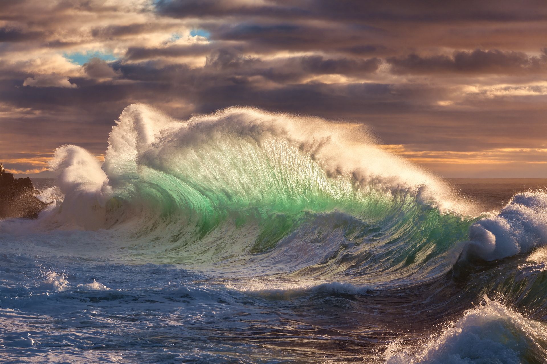 The crashing ocean sends up a curtain of green tinged water with white mist billowing from the edge of the wave.