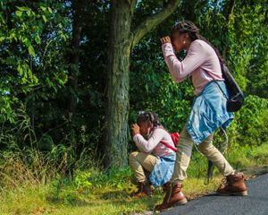 Two young people looking through binoculars into a wooded area.